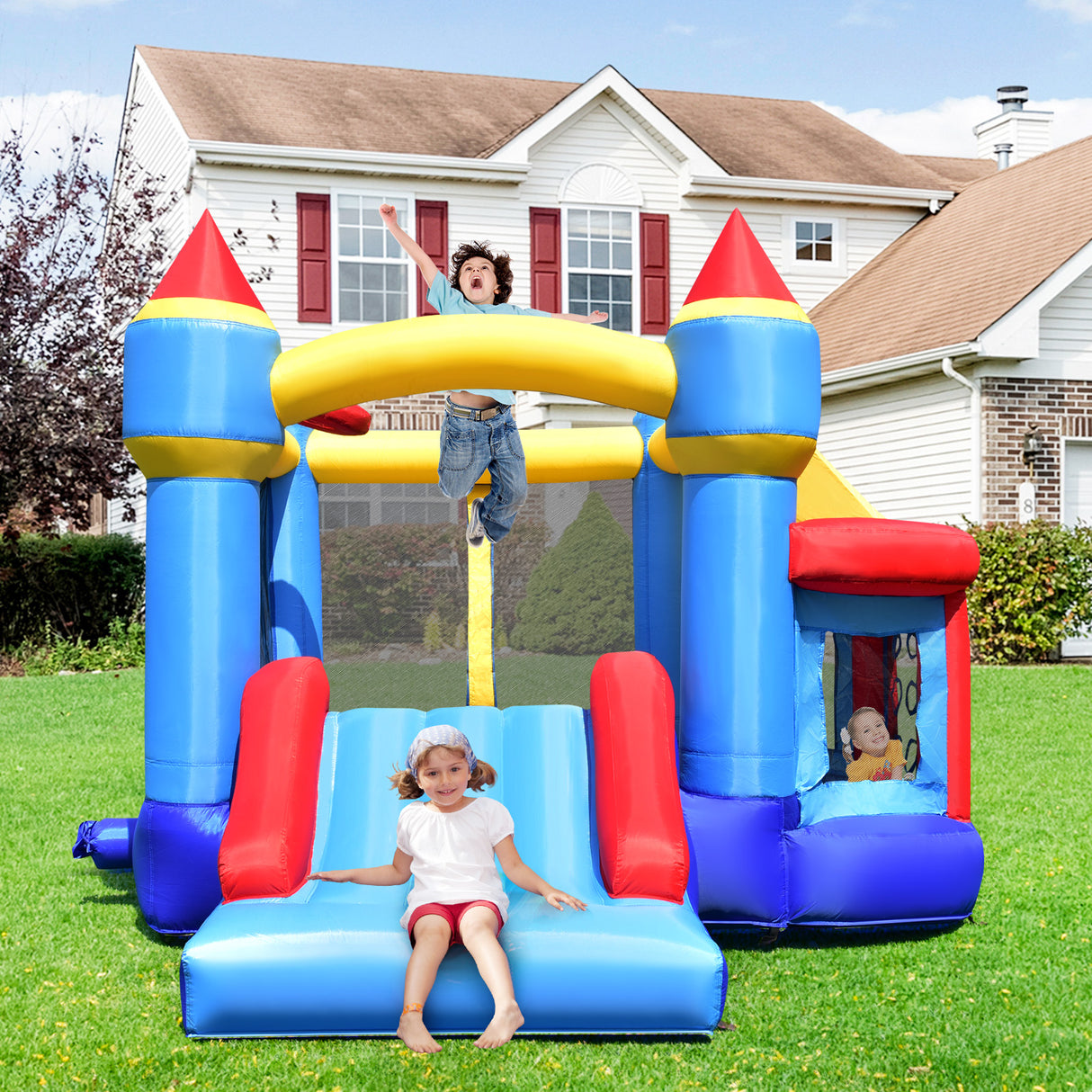 Children playing on a colorful inflatable castle bounce house in front of a house.