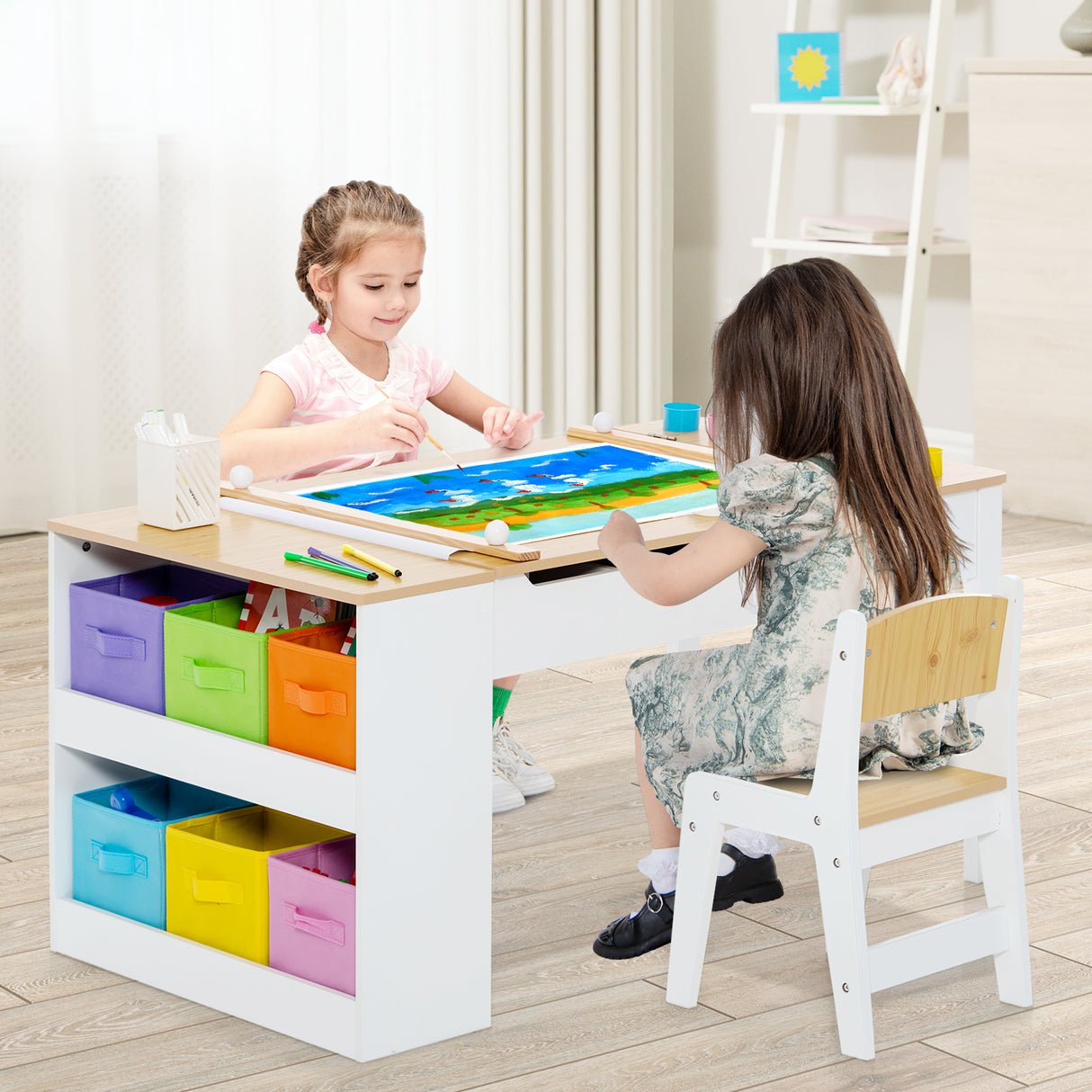 Two children sitting at a colorful children's table with storage drawers.
