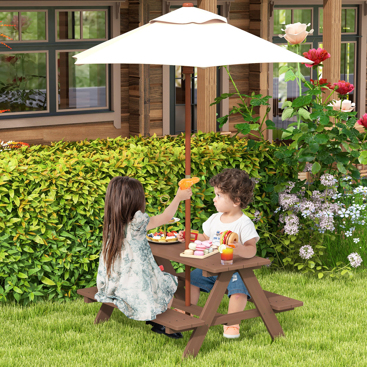 Two children at a wooden picnic table with an umbrella, surrounded by greenery and flowers.