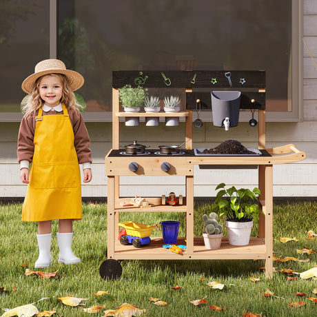 Child in a yellow apron standing next to a wooden play kitchen outdoors.