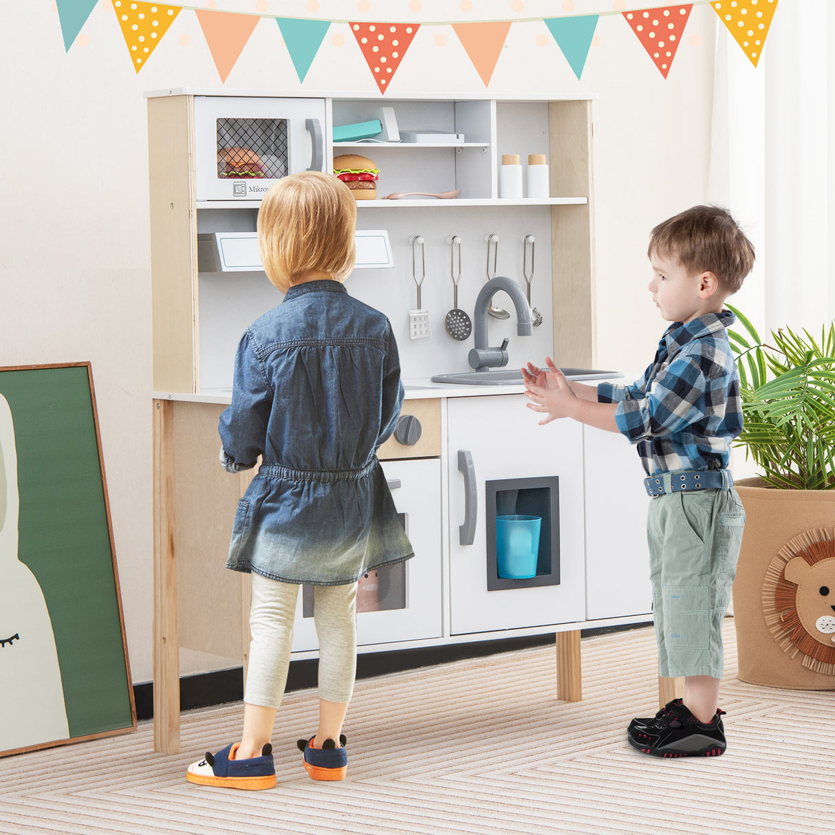 Two children playing with a toy kitchen set in a room with colorful flags on the wall.