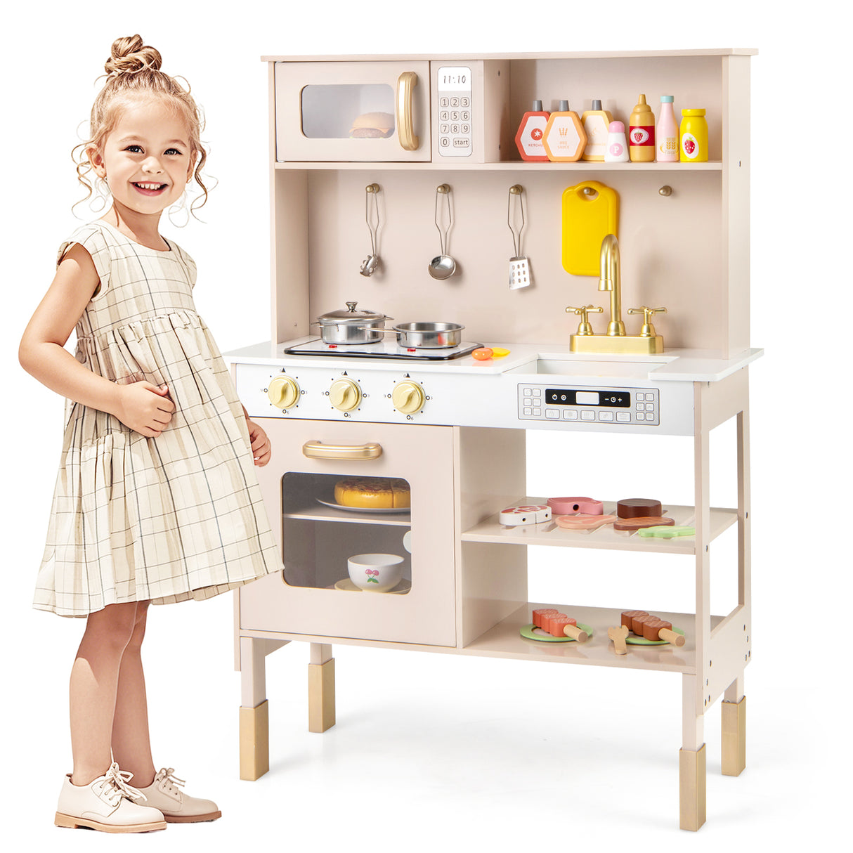 Child next to a toy kitchen set with various utensils and appliances on a white background