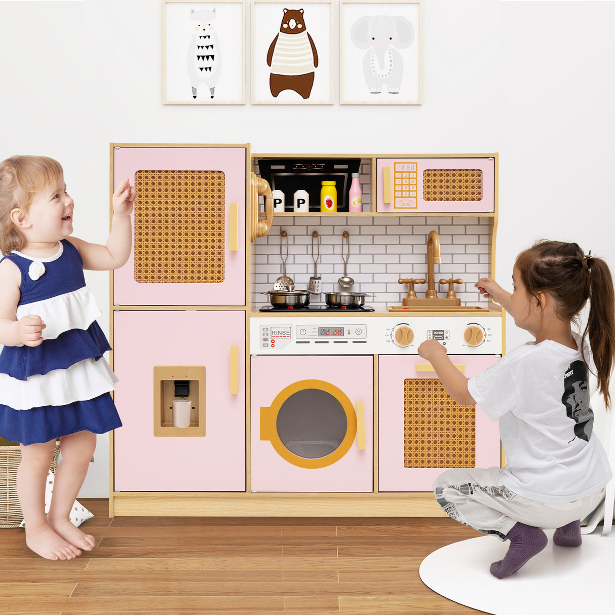 Two children playing with a pink toy kitchen set in a room with framed pictures on the wall.