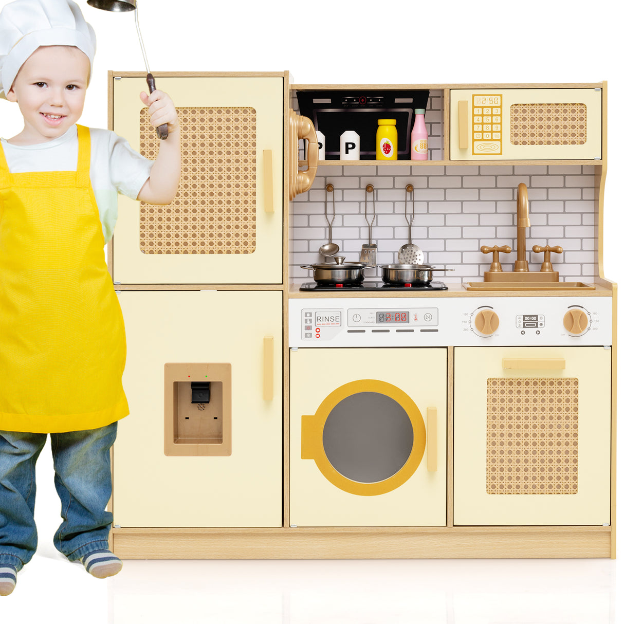 Child in a yellow apron standing next to a toy kitchen set with various appliances.