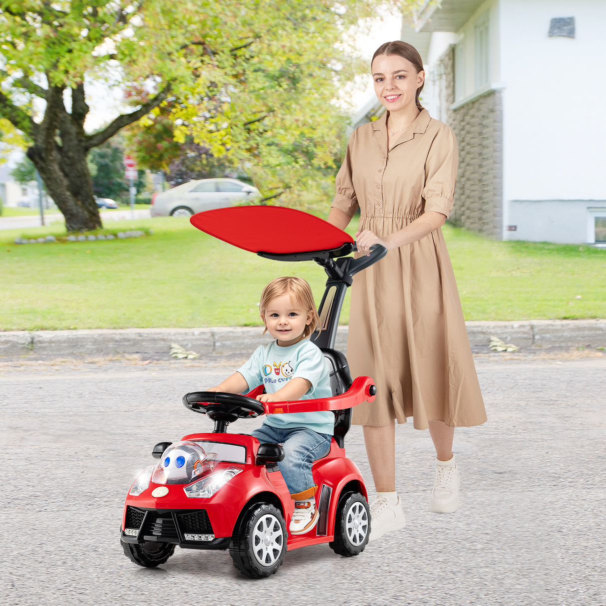 Woman pushing a child in a red toy car on a street.
