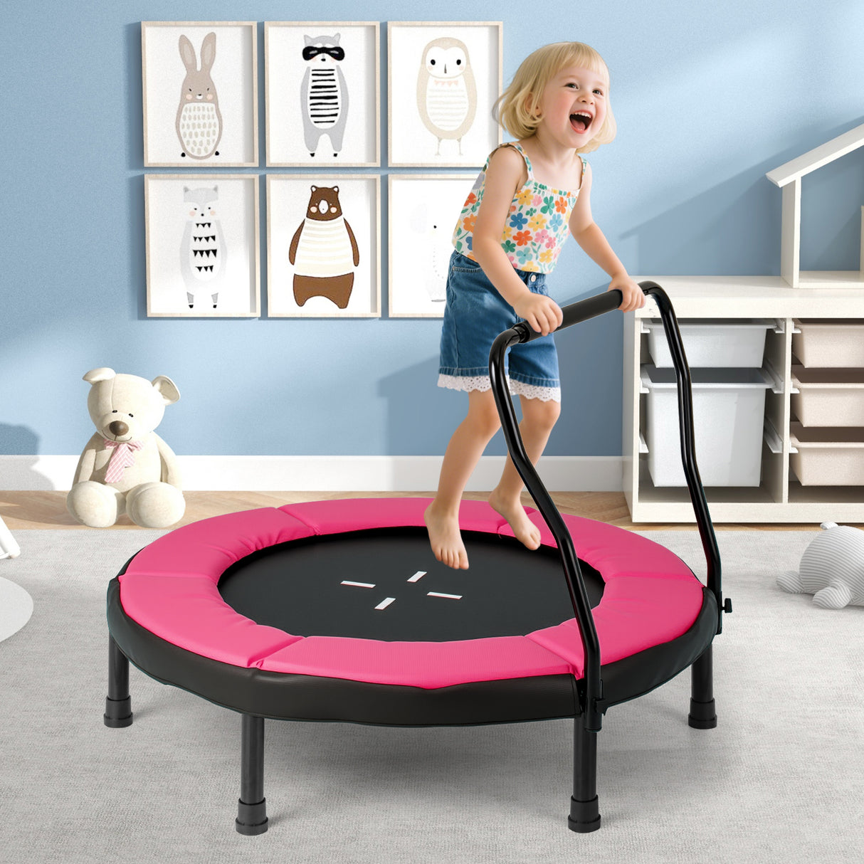 Child playing on a pink and black trampoline in a room with colorful wall art.