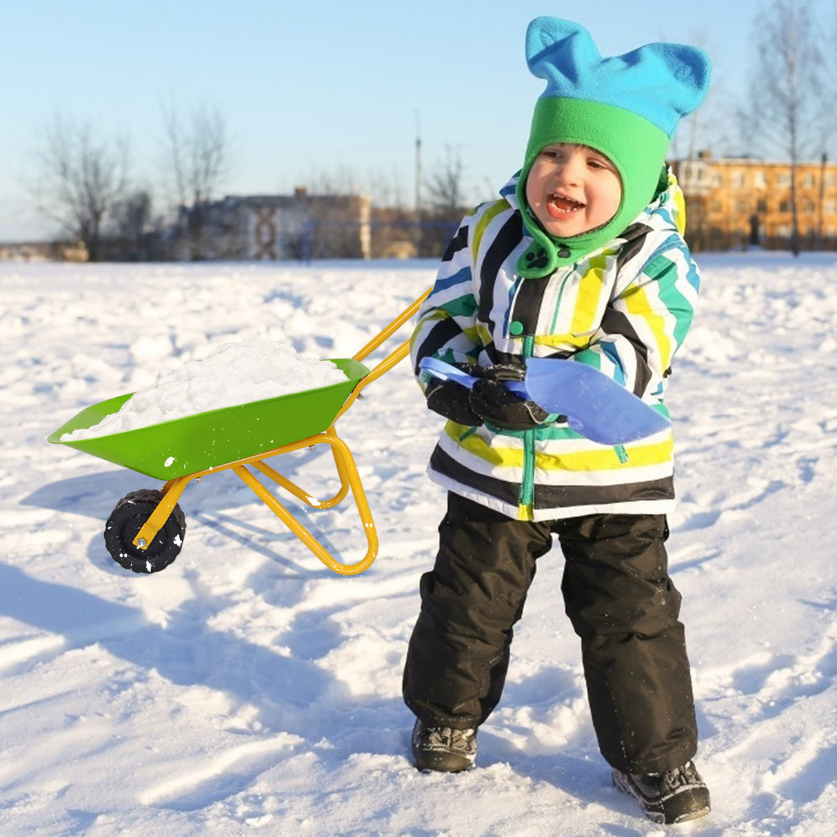 Child in winter clothing with a green wheelbarrow in a snowy landscape
