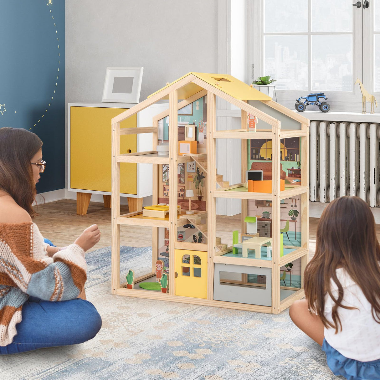Two children playing with a wooden dollhouse in a room with a blue wall and a window.