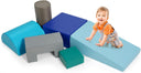 A set of colorful foam play blocks arranged on the floor with a toddler lying on top of a pink wedge block.