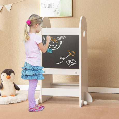Child drawing on a blackboard easel with a penguin toy nearby