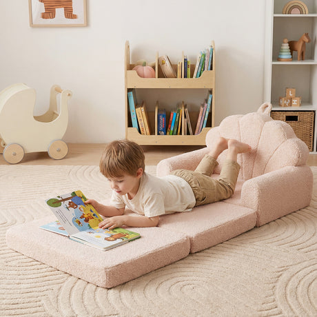 Child lying on a pink floor mat reading a book in a room with toys and books.