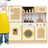 Child in a yellow apron standing next to a toy kitchen set with various appliances.