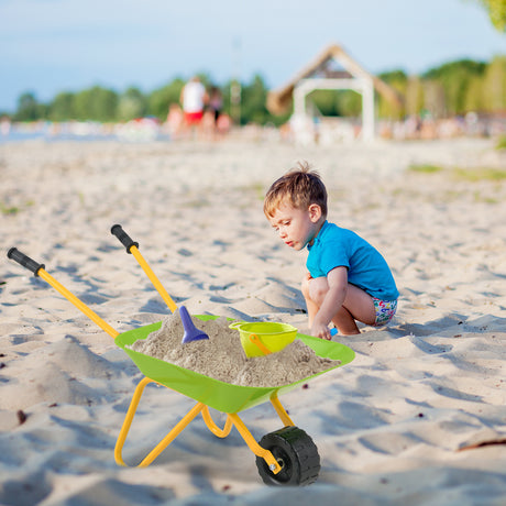 Child playing with a toy wheelbarrow and sand shovel on a sandy beach.